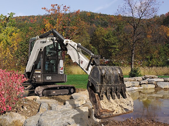 A Bobcat E35 compact excavator landscaping with an extended arm.