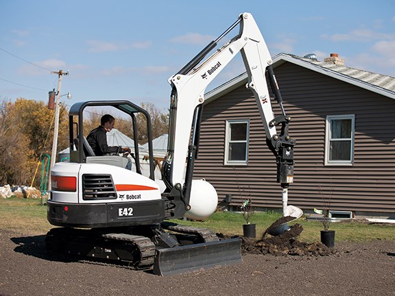 A Bobcat E42 compact excavator planting trees with an auger attachment.