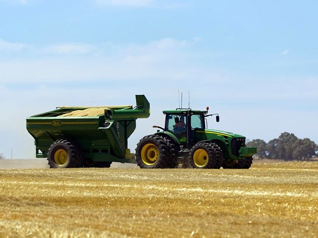 A tractor takes part in barley harvesting, alongside a combine harvester and chaser bin near Lock, on South Australia's Eyre Peninsula. Image courtesy Alamy.
